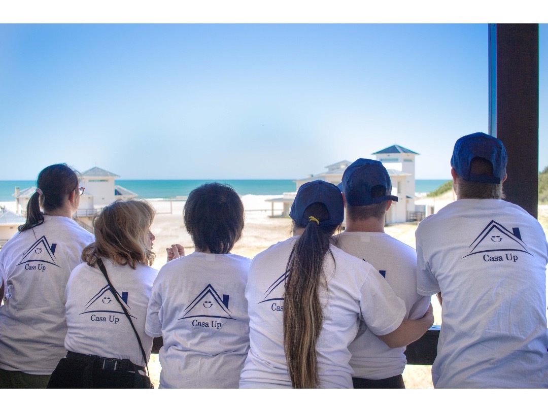 Jóvenes de Casa UP, de espaldas con remeras blancas, frente al mar